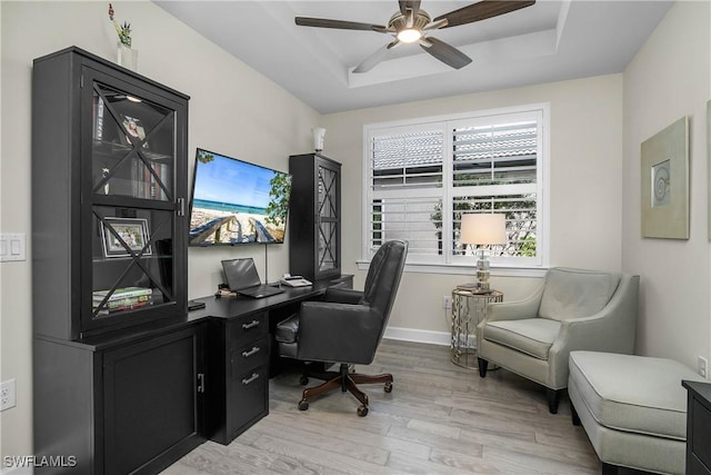 office area with light hardwood / wood-style flooring, a raised ceiling, and ceiling fan