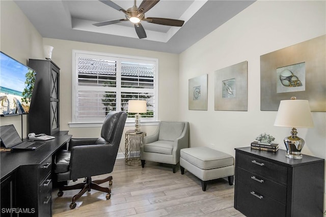 office area featuring a raised ceiling, ceiling fan, and light hardwood / wood-style flooring