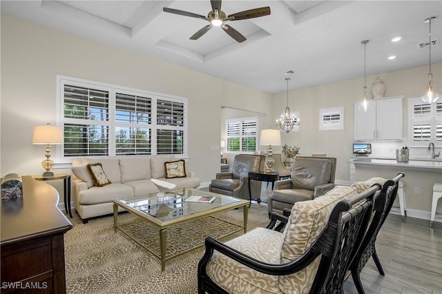 living room featuring ceiling fan with notable chandelier, sink, coffered ceiling, light hardwood / wood-style floors, and beam ceiling