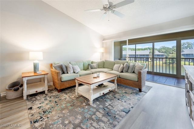 living room with a water view, vaulted ceiling, a textured ceiling, light wood-type flooring, and ceiling fan