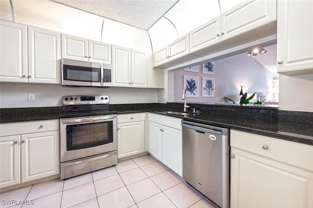 kitchen with light tile patterned flooring, appliances with stainless steel finishes, sink, white cabinets, and dark stone counters