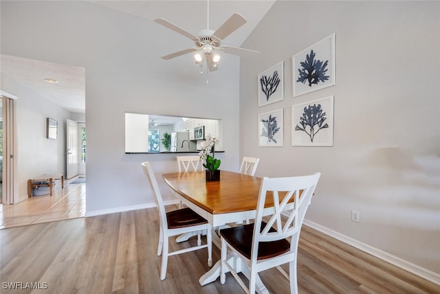 dining space featuring high vaulted ceiling, ceiling fan, and light hardwood / wood-style flooring