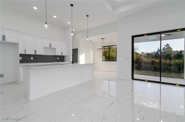 kitchen with white cabinetry, hanging light fixtures, tasteful backsplash, and a center island with sink