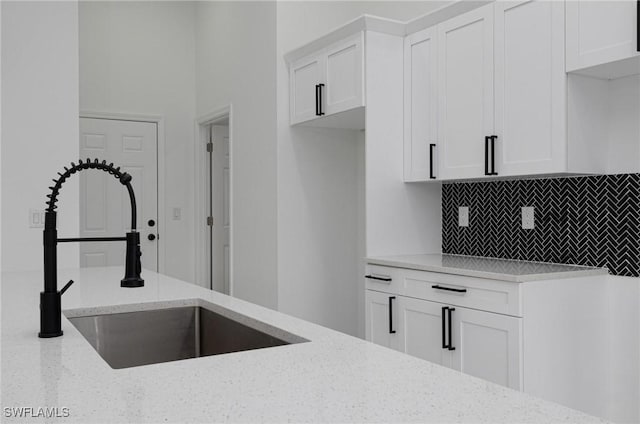 kitchen with sink, backsplash, white cabinets, and light stone counters