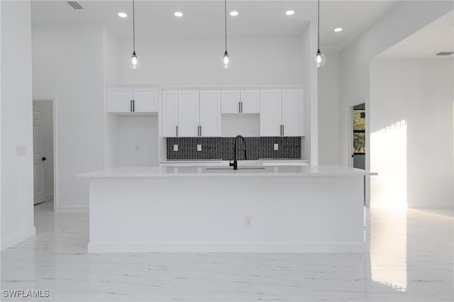 kitchen featuring pendant lighting, sink, white cabinetry, a towering ceiling, and a center island with sink