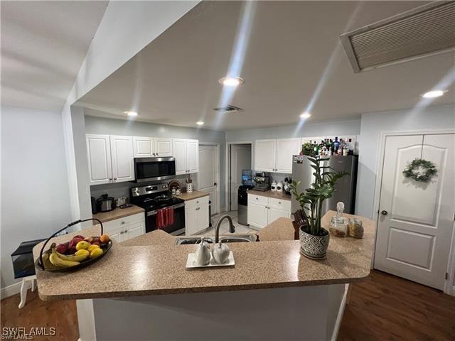 kitchen with sink, dark wood-type flooring, appliances with stainless steel finishes, backsplash, and white cabinets