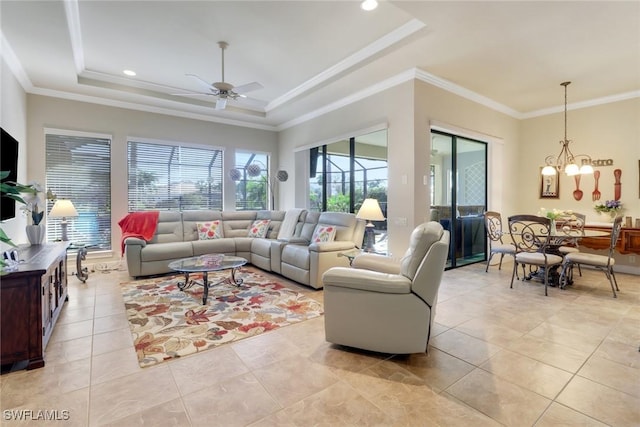 living room with ceiling fan with notable chandelier, light tile patterned floors, a tray ceiling, and ornamental molding