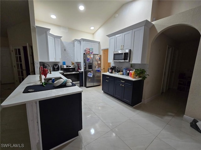 kitchen featuring sink, tasteful backsplash, white cabinetry, appliances with stainless steel finishes, and a towering ceiling