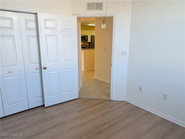 unfurnished bedroom featuring fridge, light hardwood / wood-style floors, and a closet