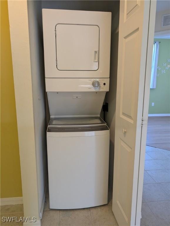 clothes washing area with stacked washer / drying machine and light tile patterned floors