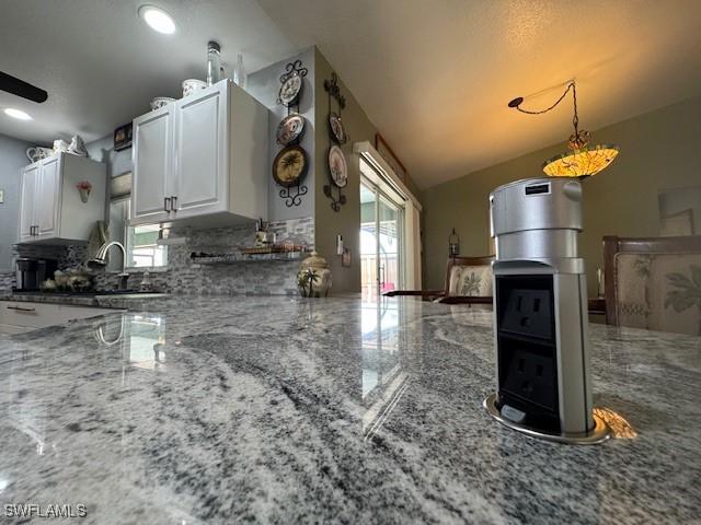 kitchen with white cabinetry, pendant lighting, vaulted ceiling, and light stone countertops