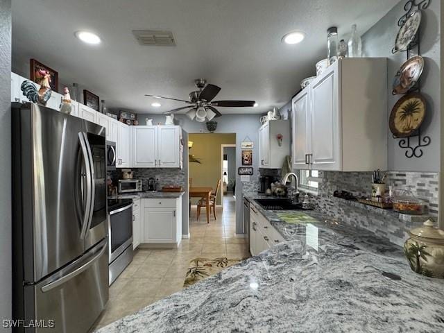 kitchen with sink, white cabinetry, dark stone countertops, light tile patterned floors, and appliances with stainless steel finishes