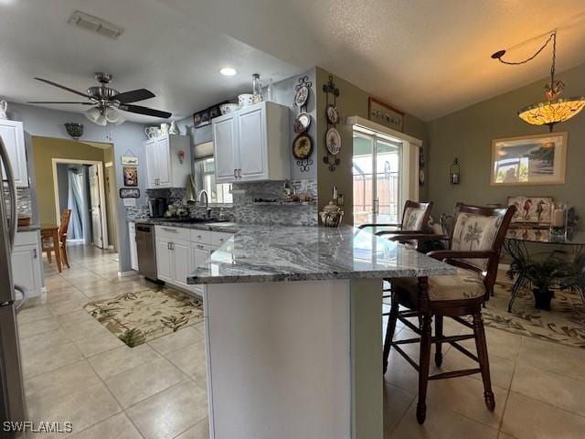 kitchen with dark stone countertops, white cabinets, decorative light fixtures, stainless steel dishwasher, and kitchen peninsula