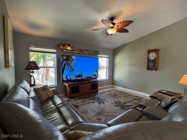 living room featuring ceiling fan, vaulted ceiling, and a textured ceiling