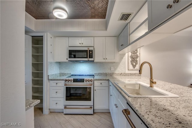 kitchen featuring a raised ceiling, white cabinetry, high end white range oven, and sink