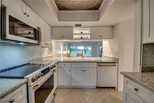 kitchen with white cabinetry, sink, white appliances, and a tray ceiling