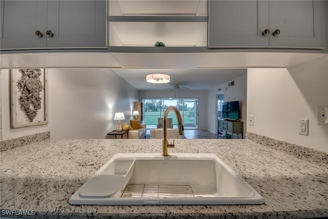 kitchen with gray cabinets, ceiling fan, sink, and light stone counters