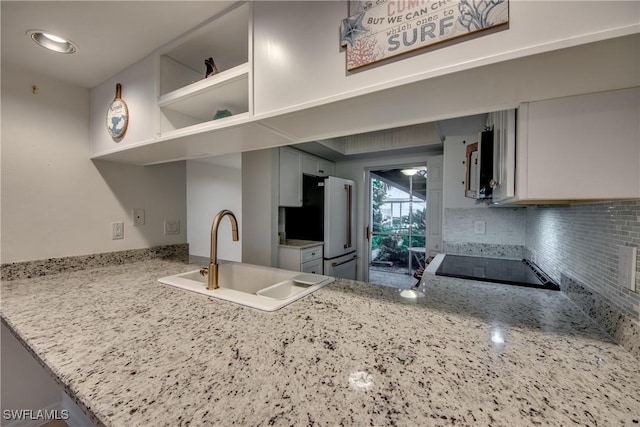 kitchen with sink, white cabinets, white fridge, light stone counters, and kitchen peninsula