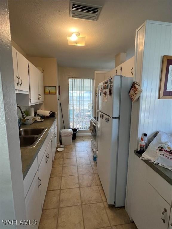 kitchen featuring white cabinetry, sink, white fridge, light tile patterned floors, and a textured ceiling