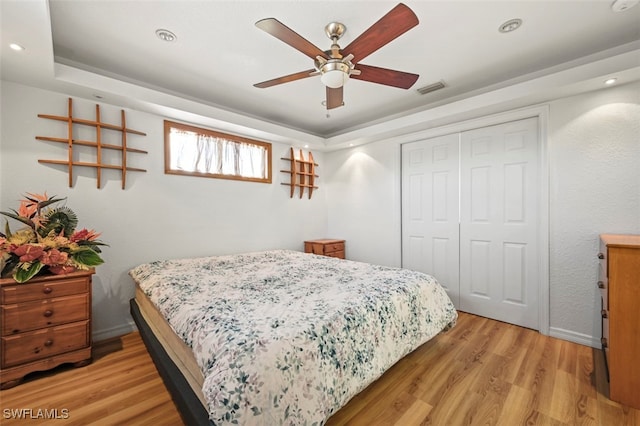 bedroom featuring a tray ceiling, light hardwood / wood-style floors, a closet, and ceiling fan