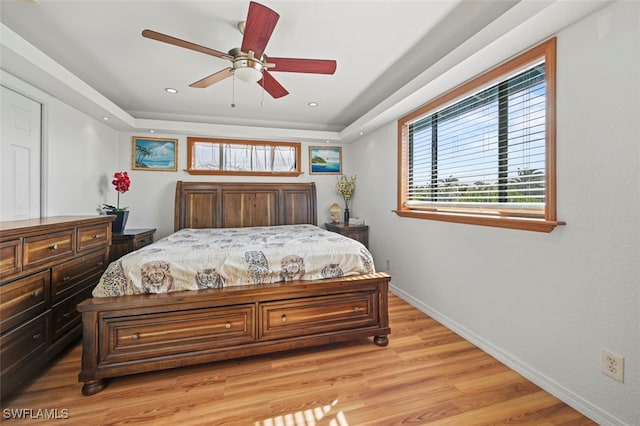 bedroom featuring a raised ceiling, ceiling fan, and light hardwood / wood-style flooring