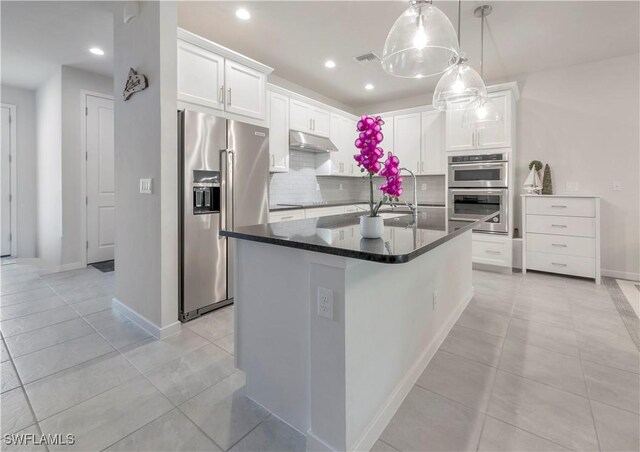 kitchen with a kitchen island with sink, backsplash, white cabinets, and appliances with stainless steel finishes