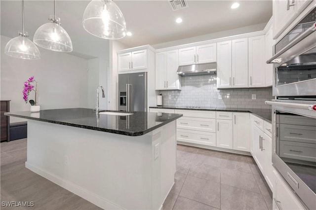 kitchen with white cabinetry, high end fridge, a kitchen island with sink, and hanging light fixtures