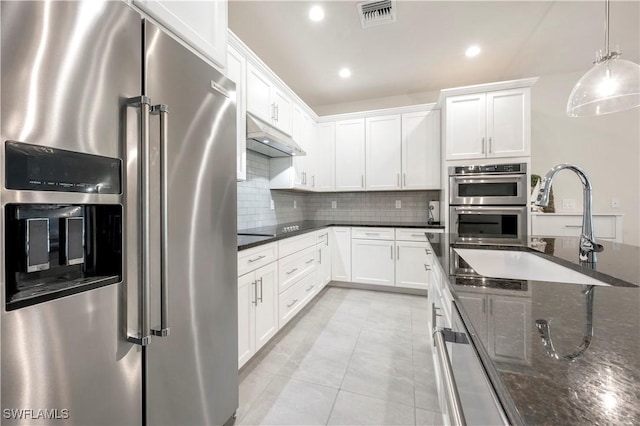 kitchen featuring white cabinetry, dark stone countertops, appliances with stainless steel finishes, pendant lighting, and backsplash