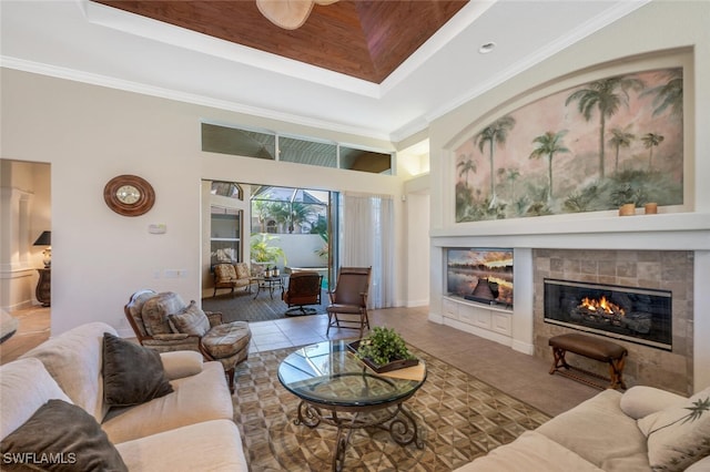 tiled living room with ornamental molding, a raised ceiling, a tile fireplace, and a high ceiling