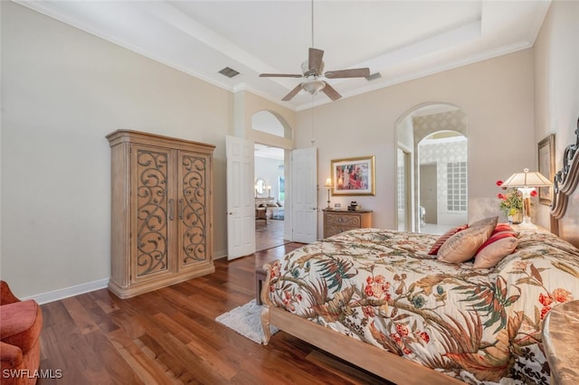 bedroom featuring ceiling fan, a high ceiling, a tray ceiling, ornamental molding, and dark hardwood / wood-style flooring