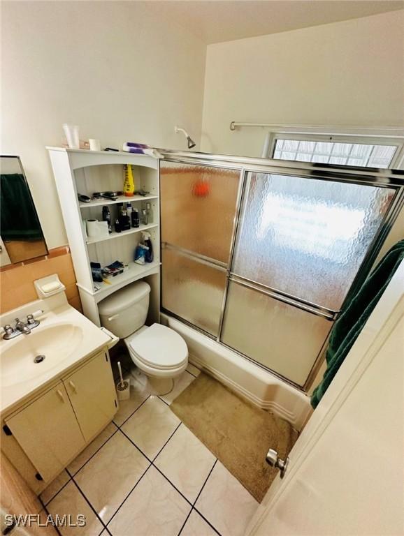 full bathroom featuring vanity, bath / shower combo with glass door, tile patterned floors, and toilet