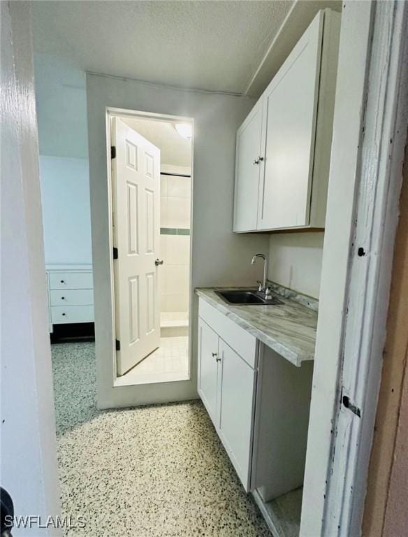 kitchen featuring light stone countertops, sink, a textured ceiling, and white cabinets