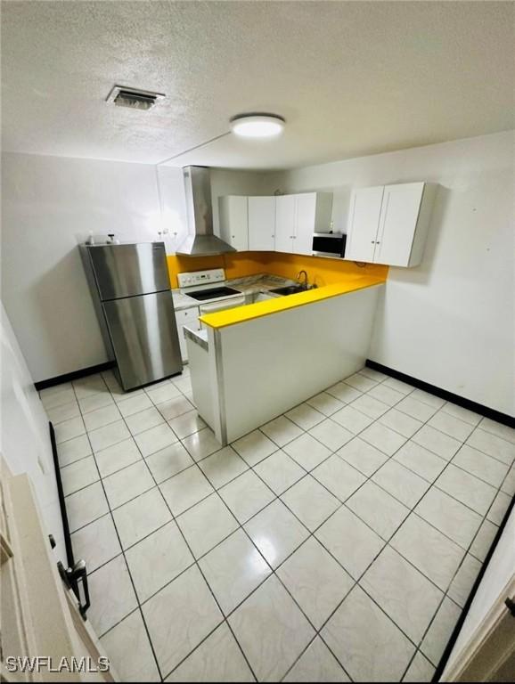 kitchen featuring wall chimney range hood, light tile patterned floors, white cabinetry, stainless steel appliances, and a textured ceiling