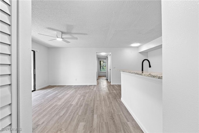 unfurnished living room with a textured ceiling, built in features, ceiling fan, and light wood-type flooring