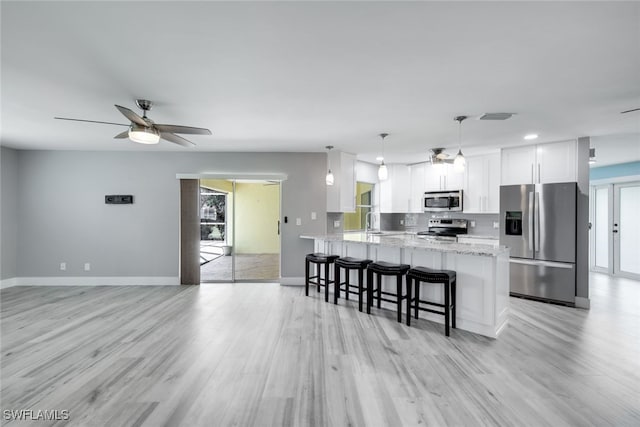 kitchen with stainless steel appliances, hanging light fixtures, white cabinetry, light stone countertops, and a peninsula