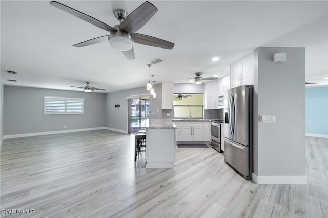 kitchen featuring white cabinets, appliances with stainless steel finishes, open floor plan, light stone counters, and decorative light fixtures