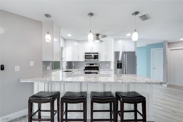 kitchen with a peninsula, white cabinets, stainless steel appliances, and decorative light fixtures