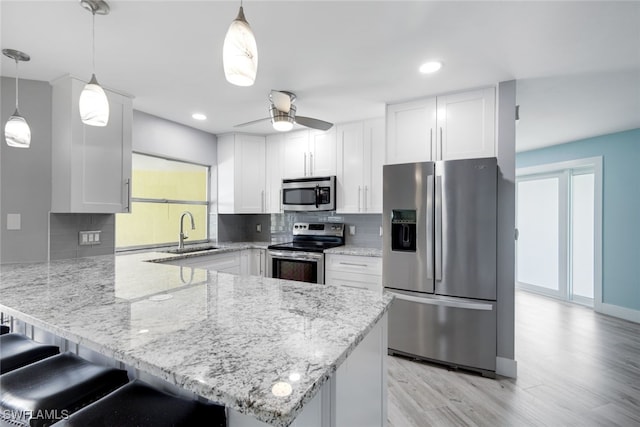 kitchen with a breakfast bar area, appliances with stainless steel finishes, hanging light fixtures, white cabinetry, and a sink