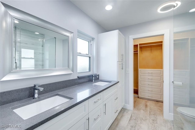 full bathroom with a spacious closet, double vanity, a stall shower, and a sink