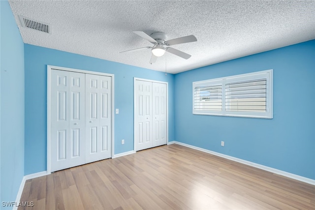 unfurnished bedroom featuring light wood-type flooring, baseboards, visible vents, and multiple closets