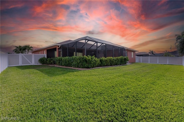 yard at dusk featuring glass enclosure, a fenced backyard, and a gate