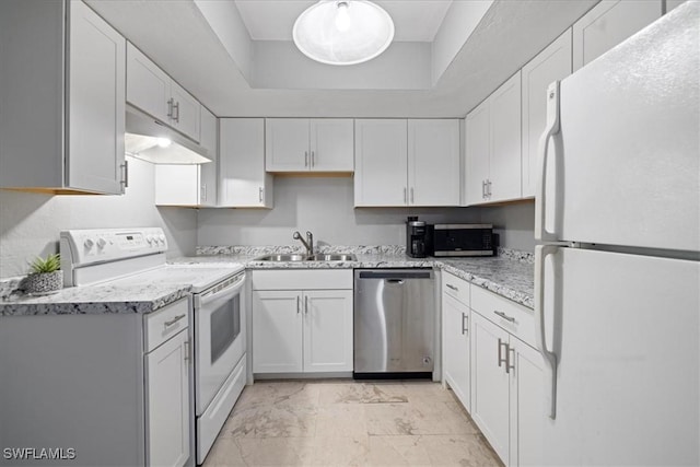 kitchen featuring sink, appliances with stainless steel finishes, a tray ceiling, light stone countertops, and white cabinets