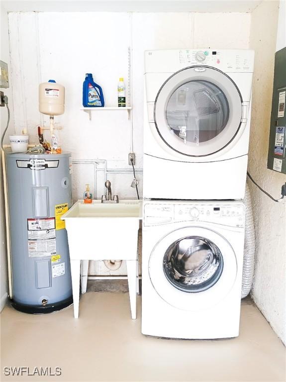 clothes washing area featuring stacked washer / drying machine, sink, and water heater