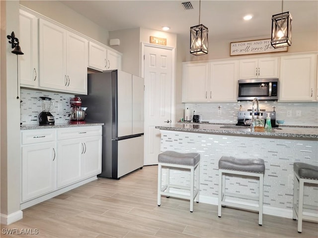 kitchen featuring white cabinetry, appliances with stainless steel finishes, decorative light fixtures, and light stone countertops