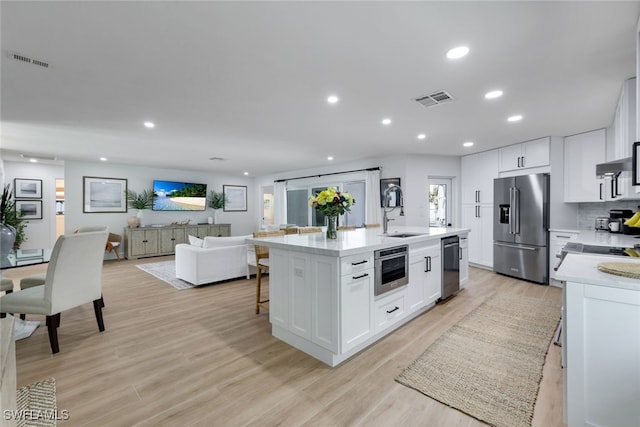 kitchen featuring white cabinetry, light wood-type flooring, an island with sink, and appliances with stainless steel finishes