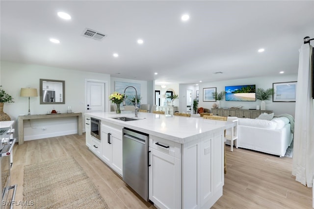 kitchen featuring sink, a kitchen island with sink, light hardwood / wood-style floors, white cabinets, and stainless steel dishwasher