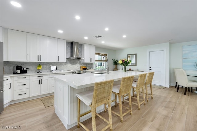 kitchen featuring wall chimney range hood, sink, a breakfast bar area, an island with sink, and white cabinets