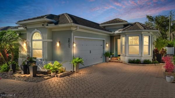 view of front facade featuring decorative driveway, a tiled roof, an attached garage, and stucco siding