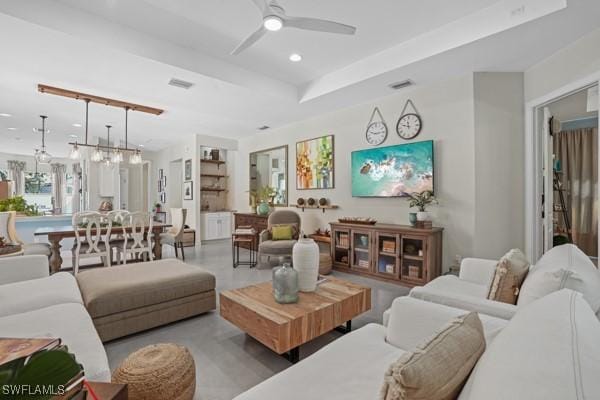 living area with a raised ceiling, recessed lighting, visible vents, and ceiling fan