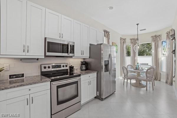 kitchen with dark stone countertops, stainless steel appliances, white cabinetry, decorative light fixtures, and tasteful backsplash